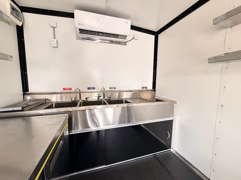 Three-compartment sink and handwash station in one stainless bank across the front wall, mini-split above